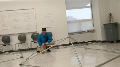 A person holding a section of assembled metal tubing in a pentagon shape.