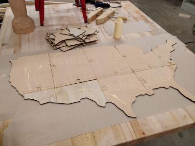 Single plywood layer in the shape of the US with glue drizzled on top.
