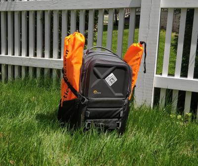 A backpack sitting in grass with four orange gate bundles, two attached to each side.